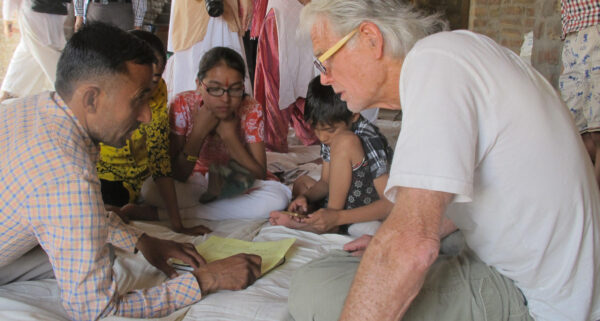 Issues in Fair Trade and Equity: someone stoops to examine another's work while sitting on the ground crosslegged